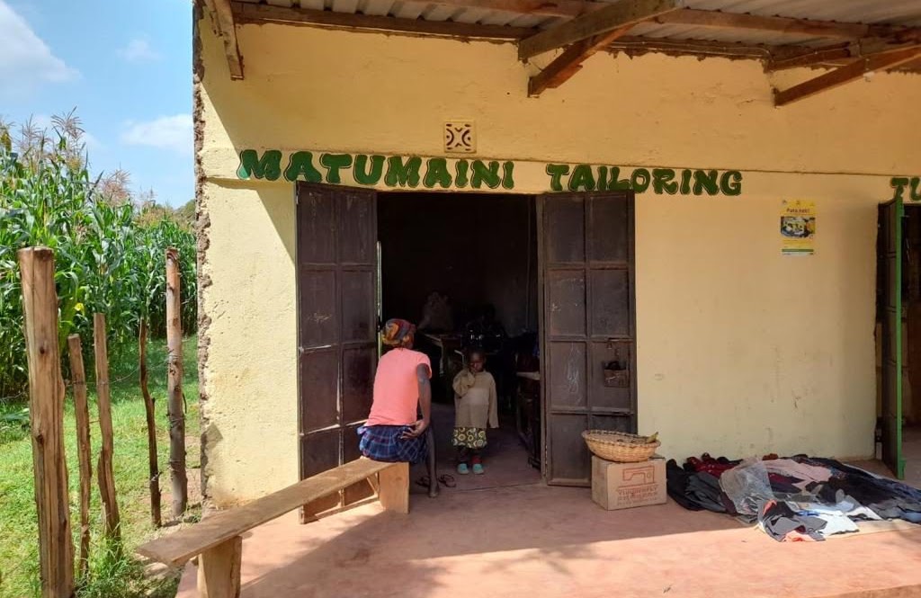 Het naaiatelier 'Matumaini Tailoring' in Kiminini, met een naaister en een kind bij de ingang